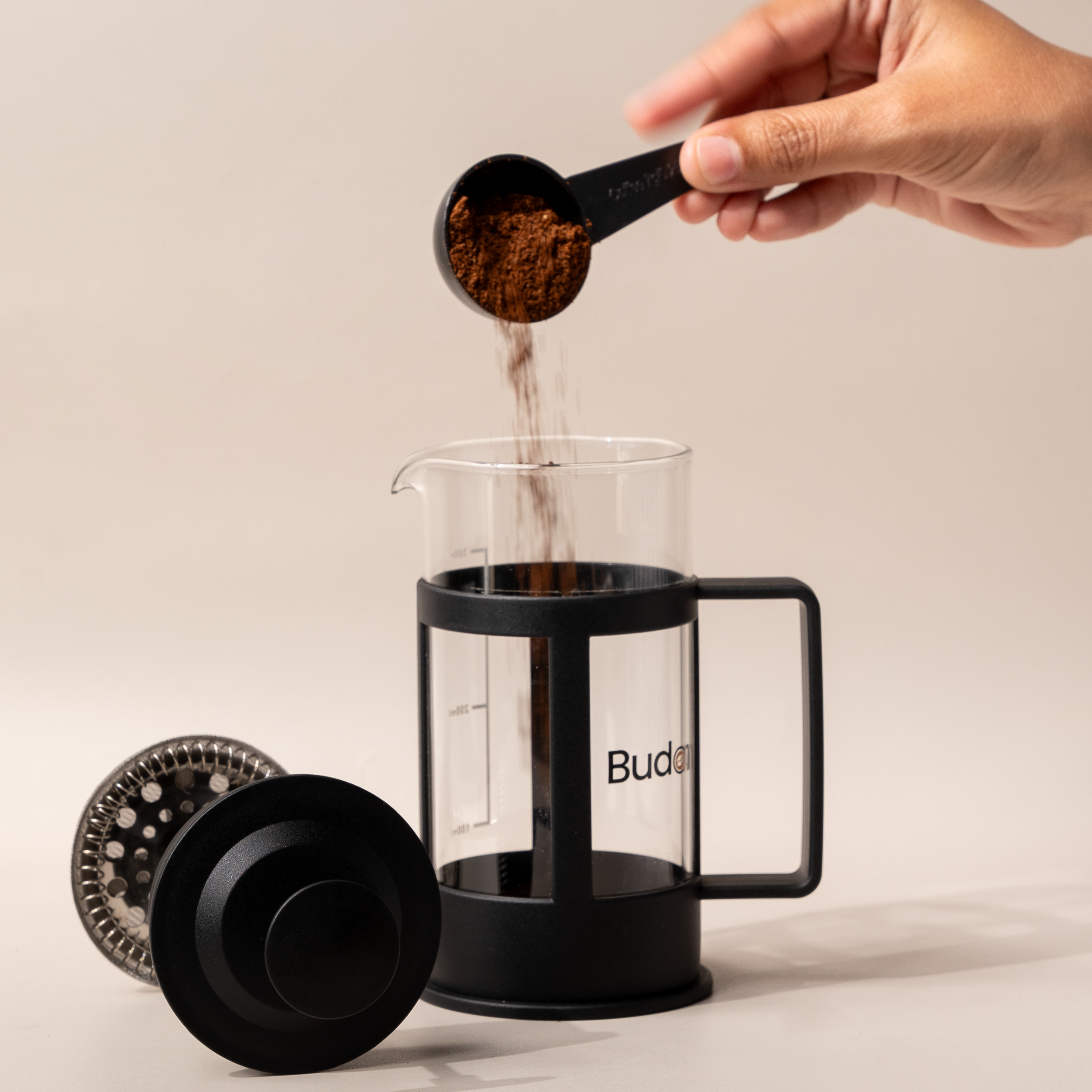 Hand pouring ground coffee into a Budapresso French press, ready for brewing fresh specialty coffee.