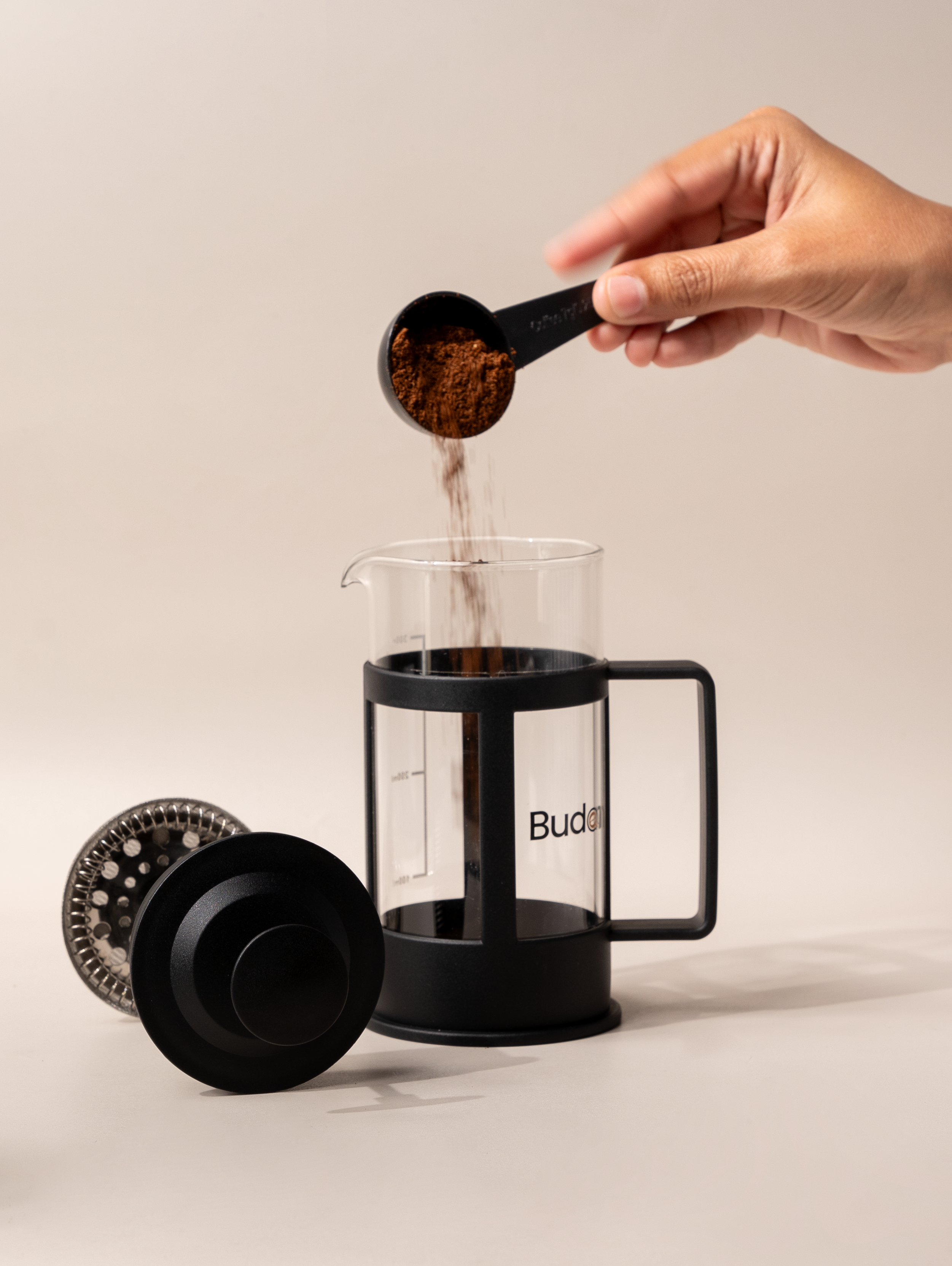 Hand pouring ground coffee into a Budapresso French press, ready for brewing fresh specialty coffee.
