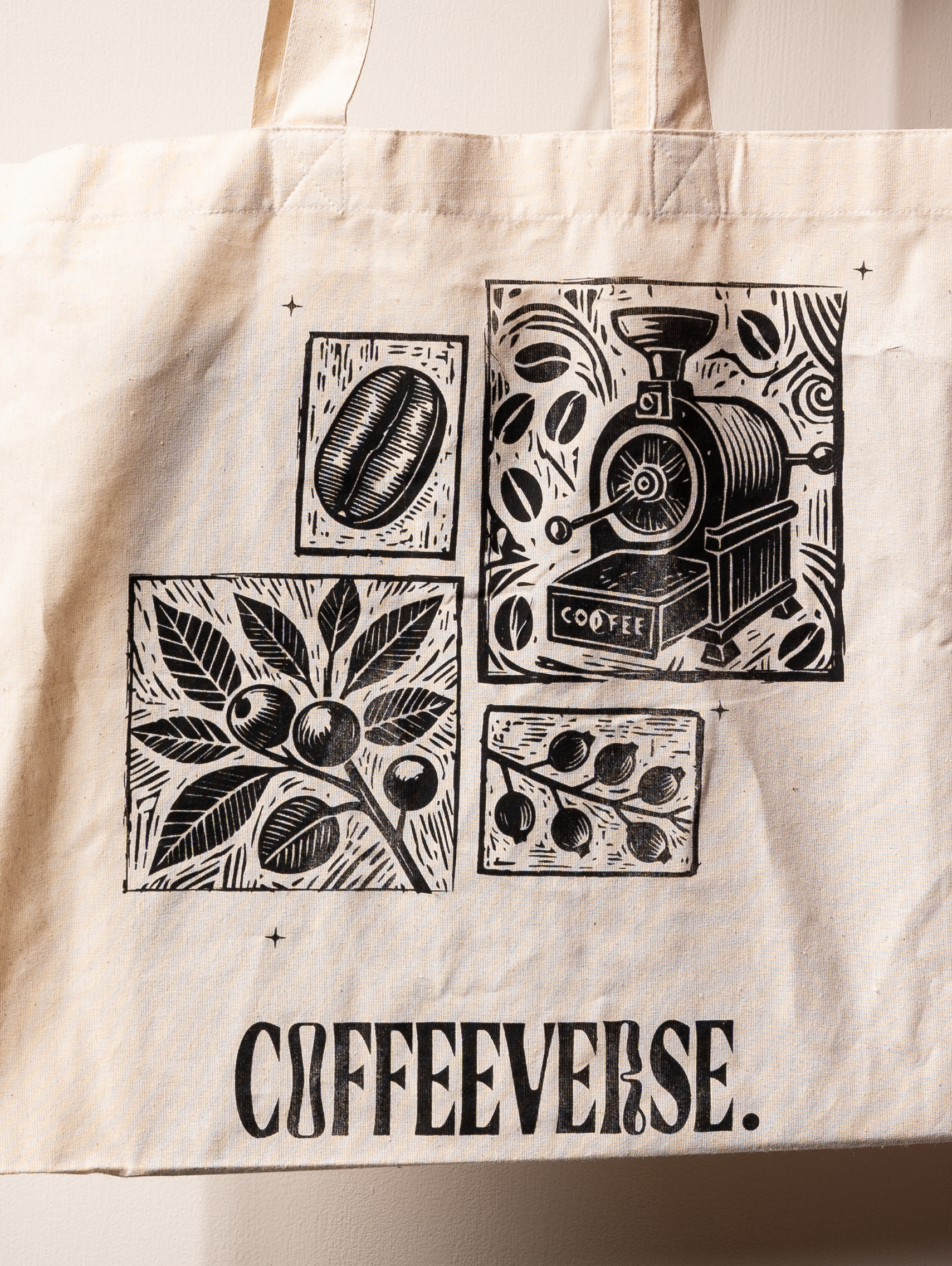 A beige cotton tote bag with black coffee-related illustrations, including a coffee bean, coffee machine, and leaves. The brand name 'COFFEEVERSE' is printed at the bottom.