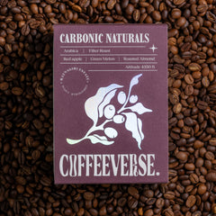A package of Carbonic Naturals coffee with a purple label, displaying the brand name and coffee variety, placed on a background of coffee beans.